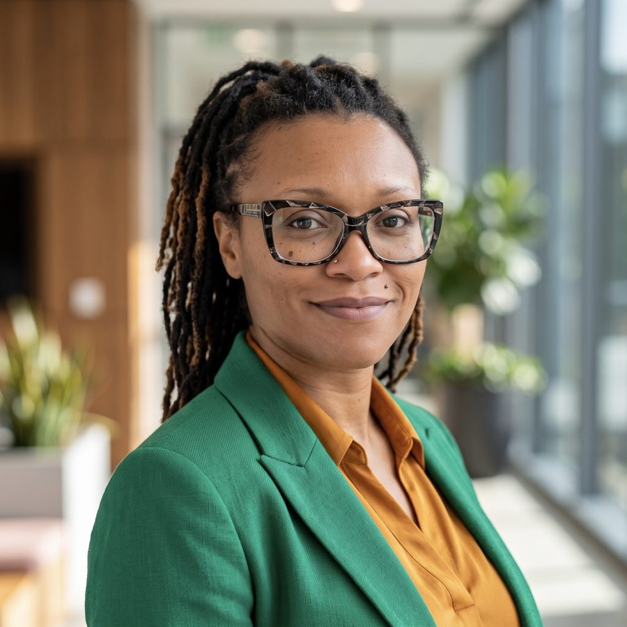 Erica Downing in an emerald blazer, gold blouse, and glasses, smiling